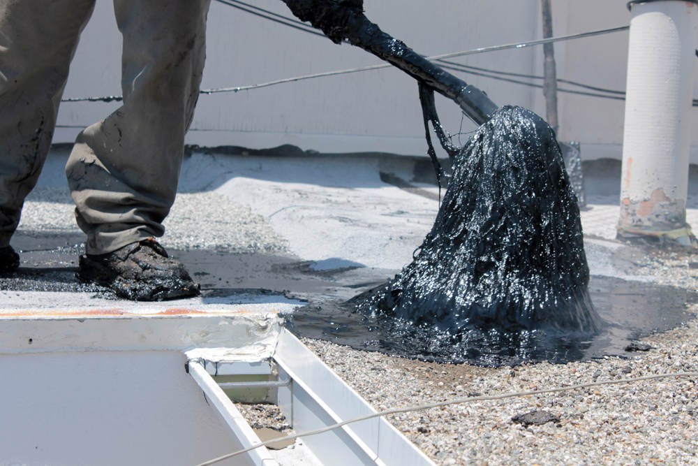 Roofer spreading molten asphalt across a flat roof with a hot mop